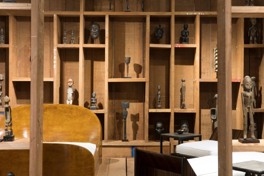 Wooden shelves displaying various African sculptures and artifacts in a warmly lit room.