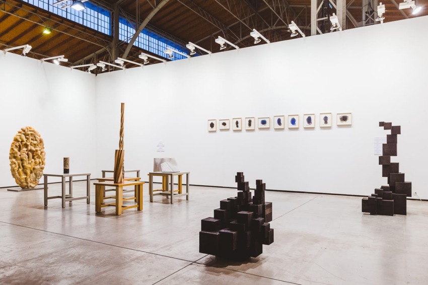 Contemporary art gallery with diverse sculptures and framed artworks displayed in a well-lit, spacious setting.