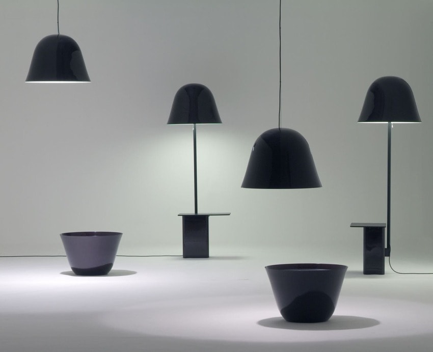 Modern black pendant, table, and floor lamps displayed in a minimalist setting with two dark bowls on the floor.