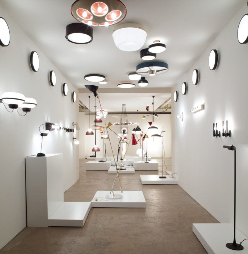 A gallery room displaying various modern light fixtures on walls and ceiling with a minimalist design.