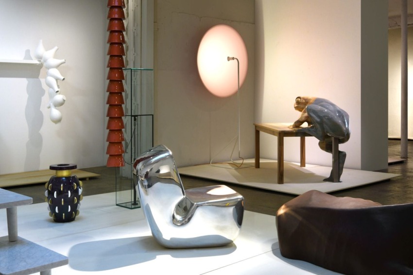 Modern art exhibition with abstract sculptures, a shiny chair, a stylized figure at a table, and various decorative pieces