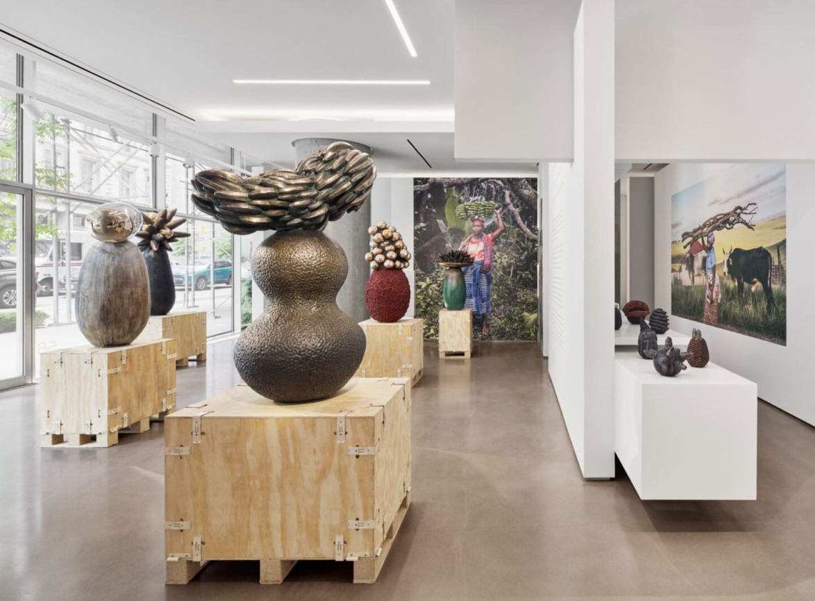 Art gallery displaying various abstract sculptures on wooden crates with large murals in the background.