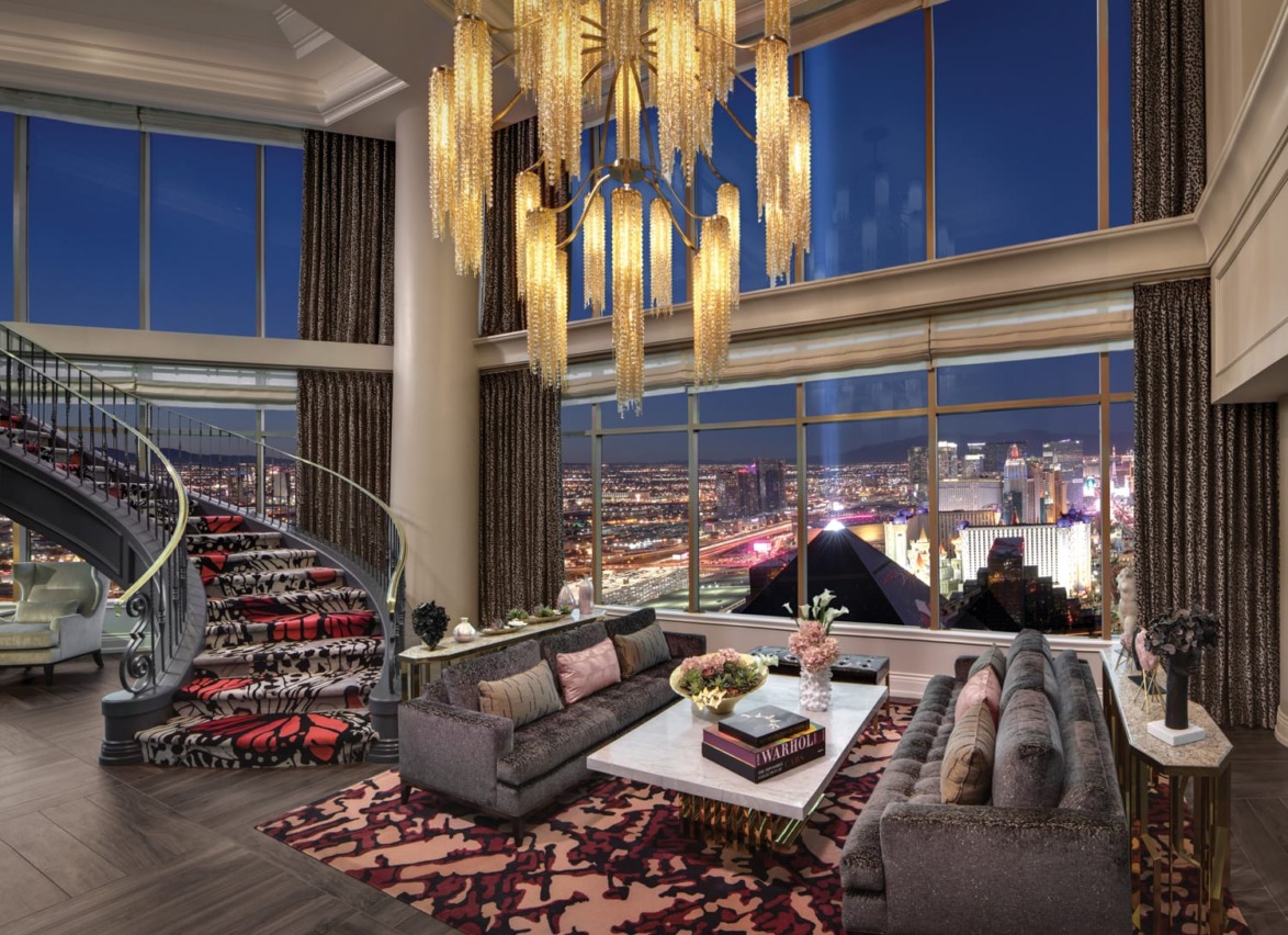 Luxurious living room with modern decor, large chandelier, and panoramic cityscape view through floor-to-ceiling windows.