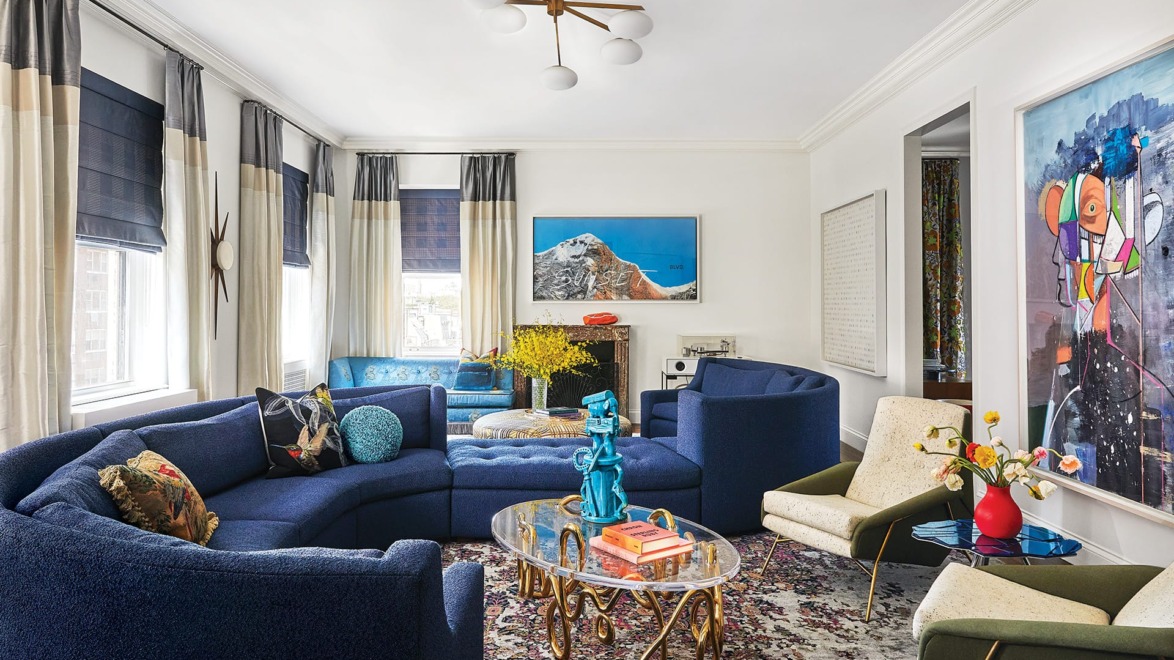 Modern living room with blue curved sofa, abstract wall art, and eclectic decor including vibrant sculptures and patterned rug.