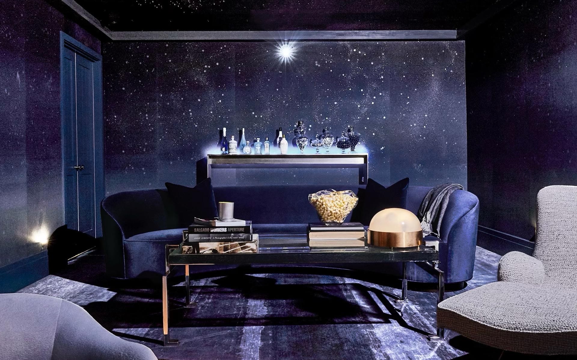 Luxurious dark room with starry walls, navy furniture, a glass coffee table with books, and elegant decor accents.