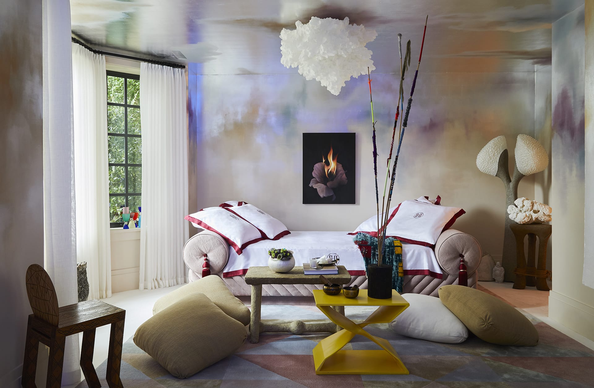 Colorful, eclectic room with abstract wall art, bright cushions, unique furniture, and large windows letting in natural light.