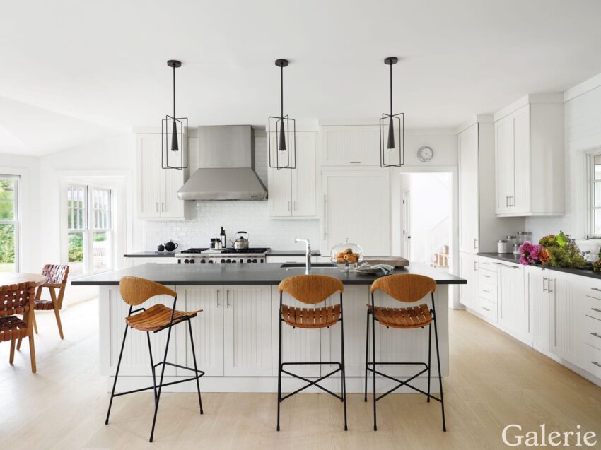 Modern white kitchen with sleek island, wooden bar stools, pendant lighting, and stainless steel appliances.