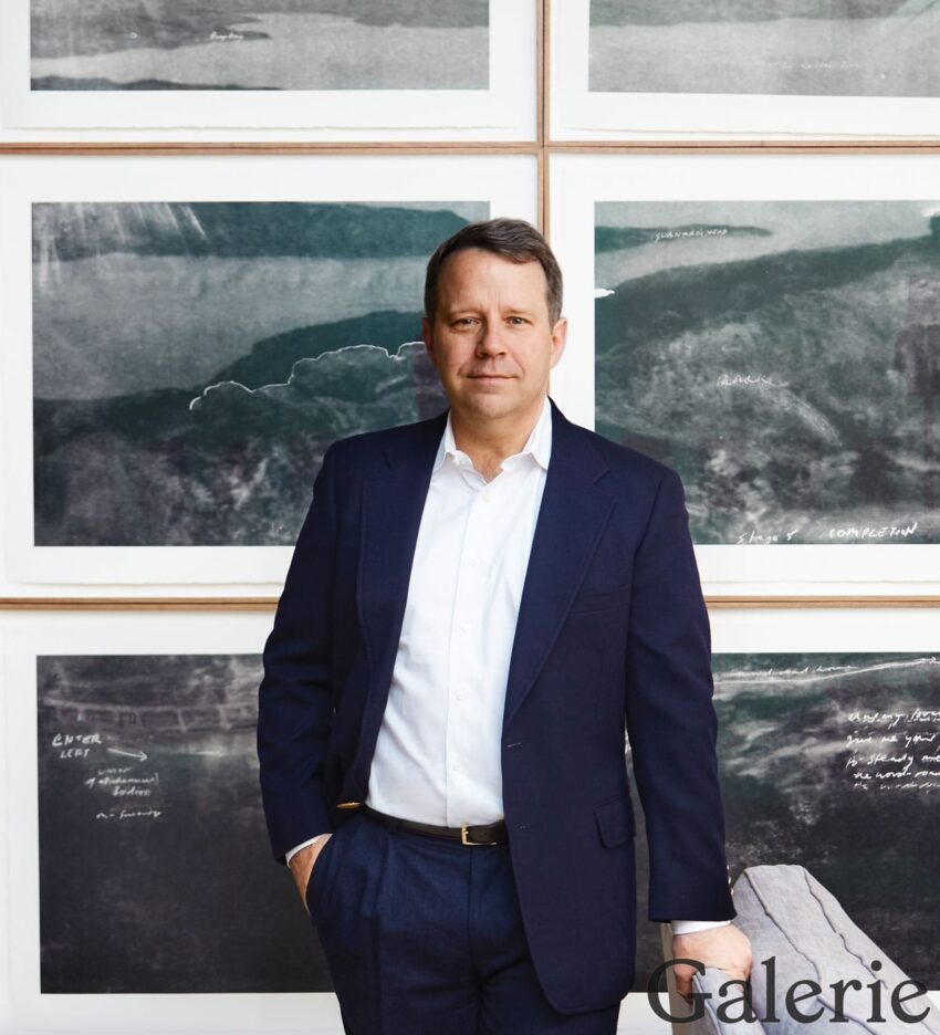 Man in a suit standing in front of framed artwork with abstract landscape on the wall.
