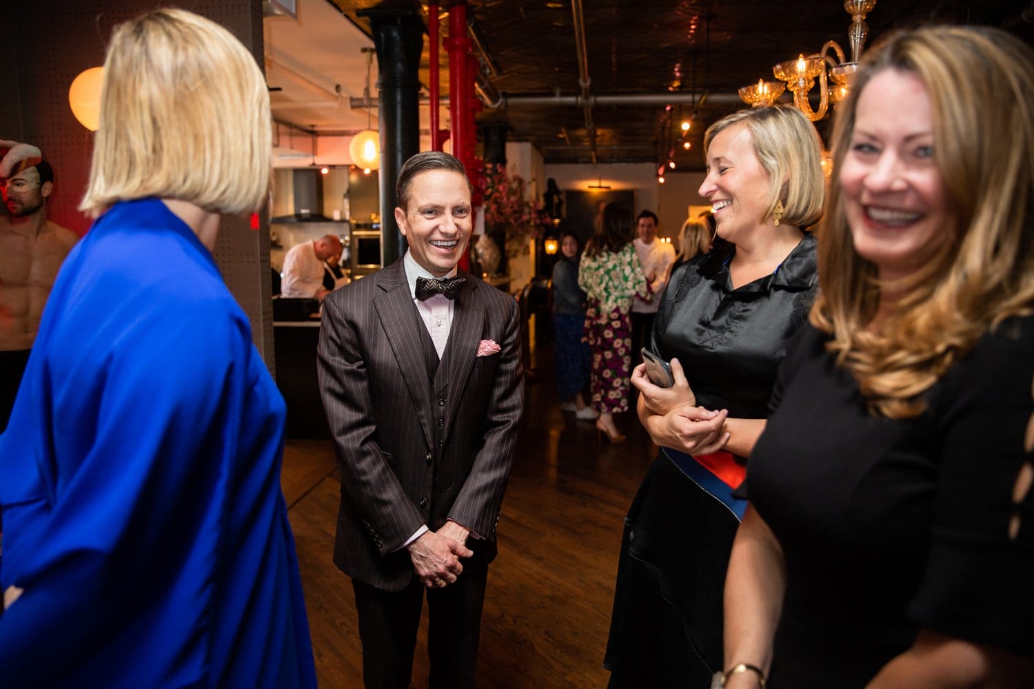 Group of people having a conversation at an indoor event with a warmly lit background.