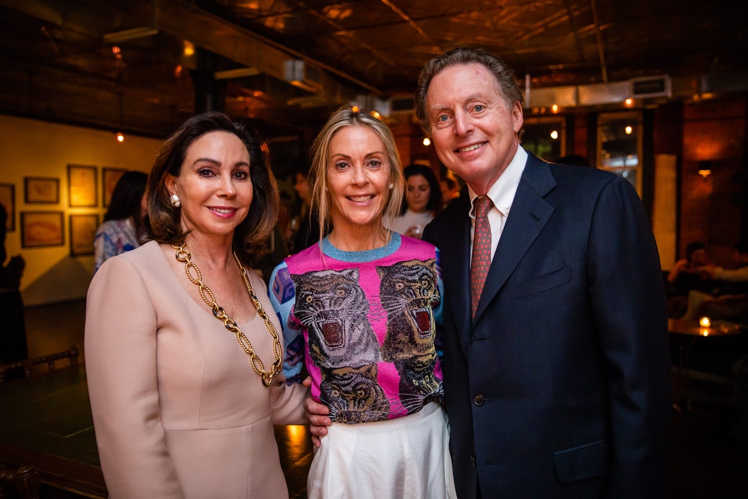 Three people smiling at an indoor event, with warm lighting and wall art in the background.