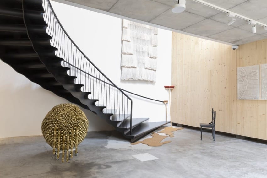 Modern interior with a spiral staircase, unique sculptures, wall art, and a black chair on a concrete floor.