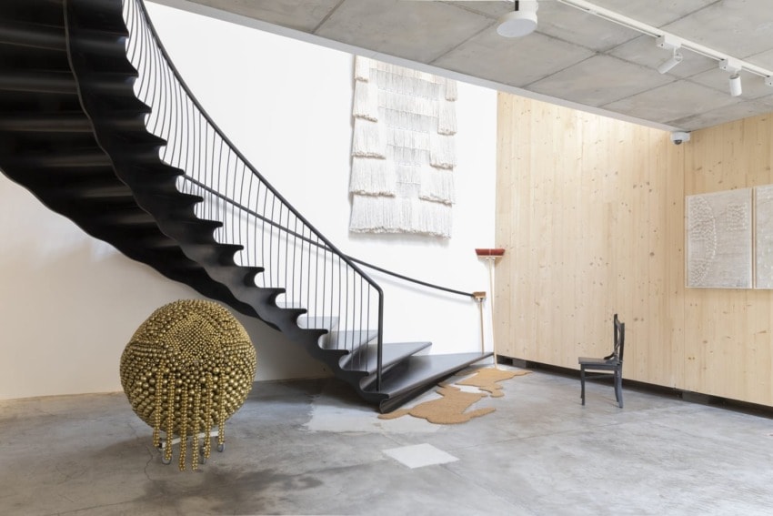 Modern interior with a spiral staircase, unique sculptures, wall art, and a black chair on a concrete floor.