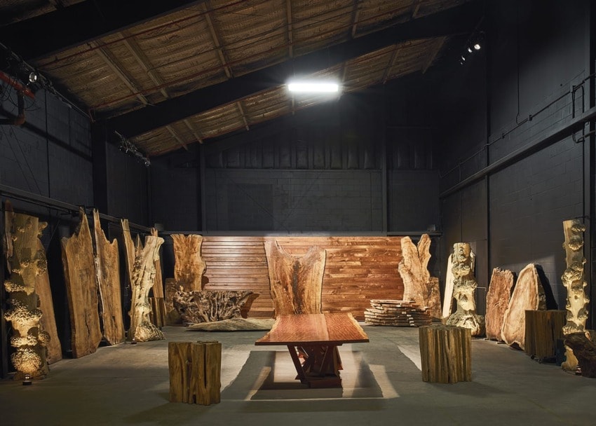 Rustic gallery with large wooden sculptures and a central wooden table illuminated in a dimly lit warehouse.