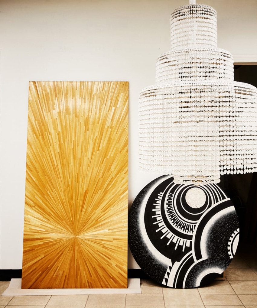 Modern art pieces with wooden sunburst design and monochrome geometric patterns next to a large crystal chandelier