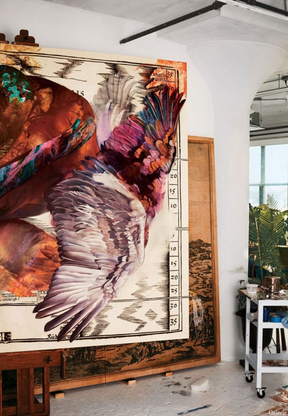 Colorful abstract painting with detailed wings, set in an artist's bright studio with tools and plants in the background.