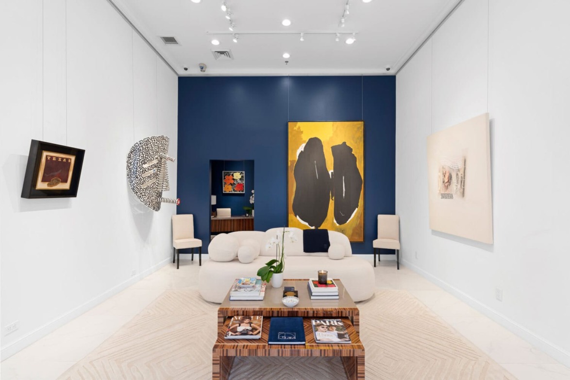 Modern art gallery with abstract paintings, sculptures, and a cozy seating area with a central coffee table and books.
