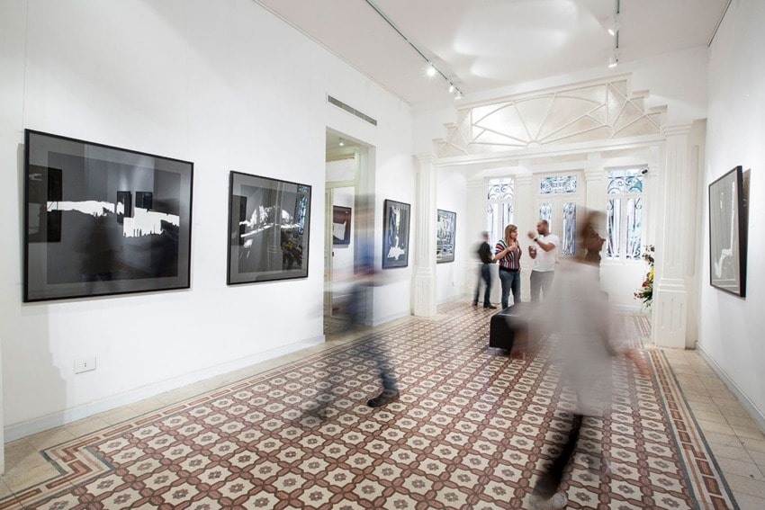 People walking through an art gallery with black and white photographs on white walls, creating a blurred motion effect.