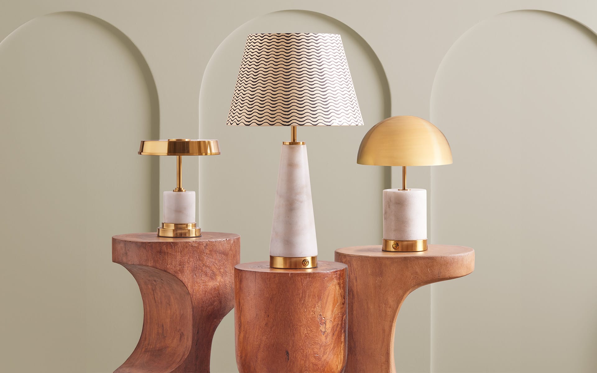 Three stylish table lamps on wooden stands with elegant designs against a soft green background.