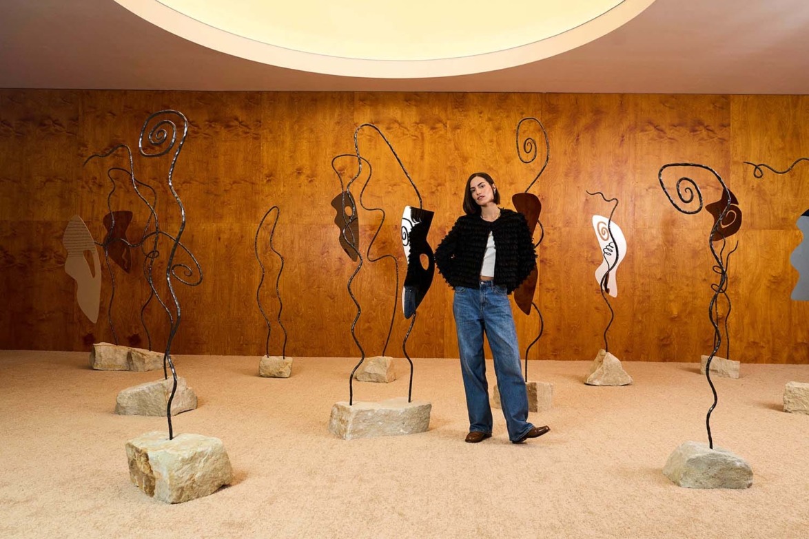 Person standing among abstract metal sculptures in a room with wooden walls and a circular ceiling light.