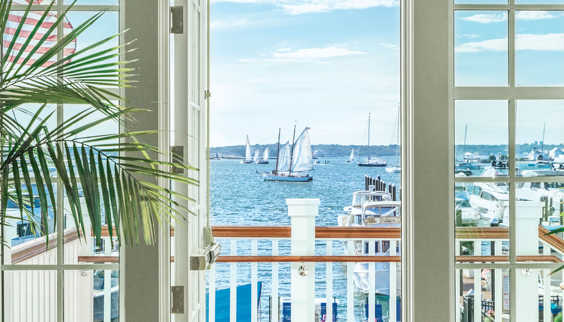View of a marina through large windows with sailing boats on a sunny day.