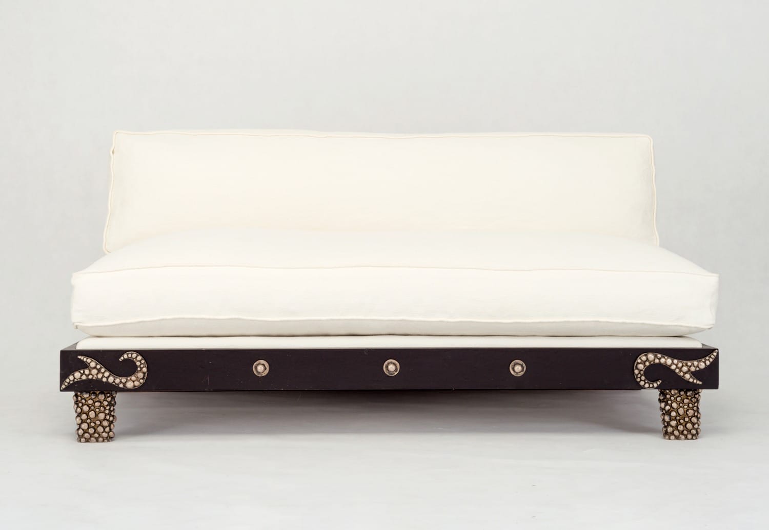 Elegant white couch with decorative black wooden base and intricately patterned legs against a neutral background.