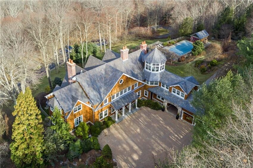 Aerial view of a large wooden house with a tower, surrounded by trees and a swimming pool in the backyard.