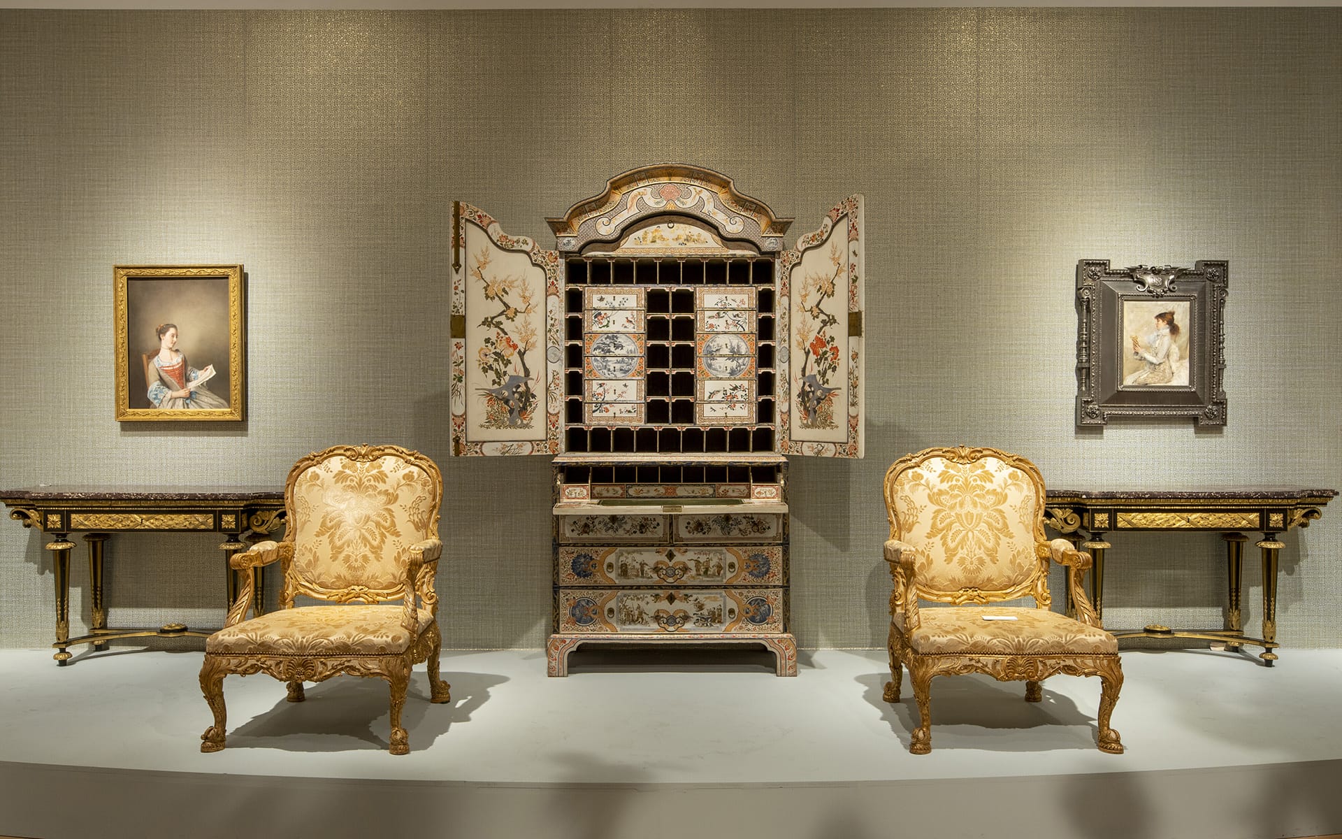Elegant antique room setup with ornate chairs, a decorative cabinet, and framed artwork on a neutral textured wall.