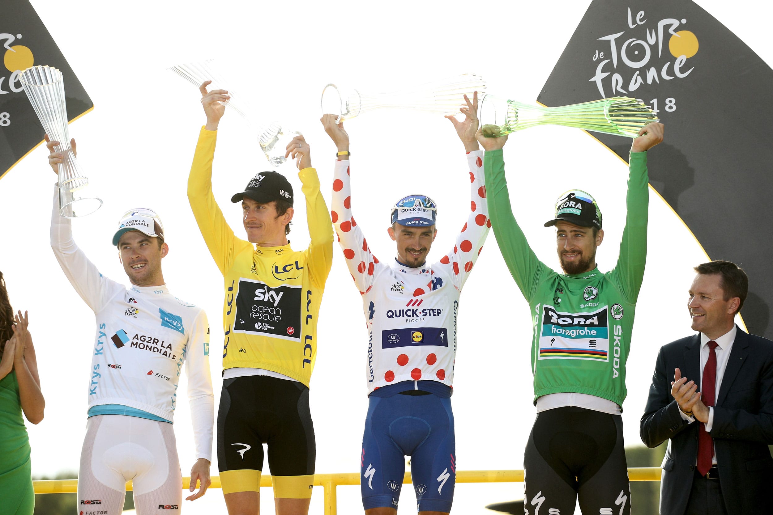 Cyclists celebrating on podium with trophies at Tour de France event.