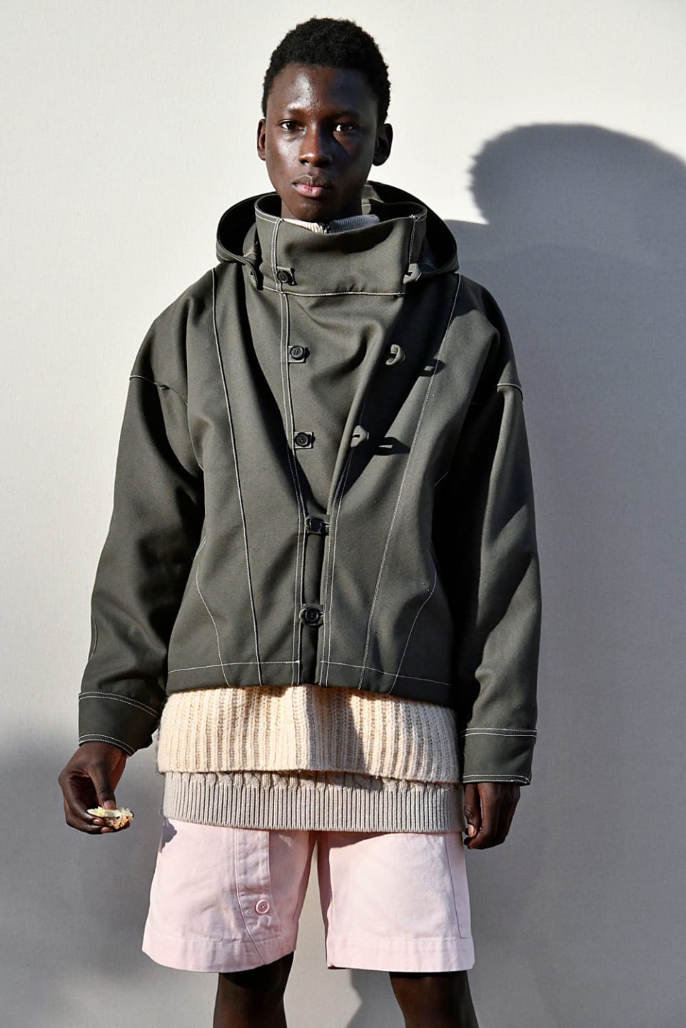 Person wearing a stylish hooded jacket with layered clothing, standing against a plain backdrop.