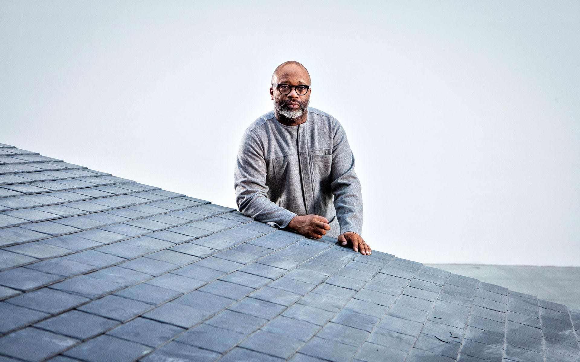 Man standing by a slanted tiled surface against a plain backdrop.