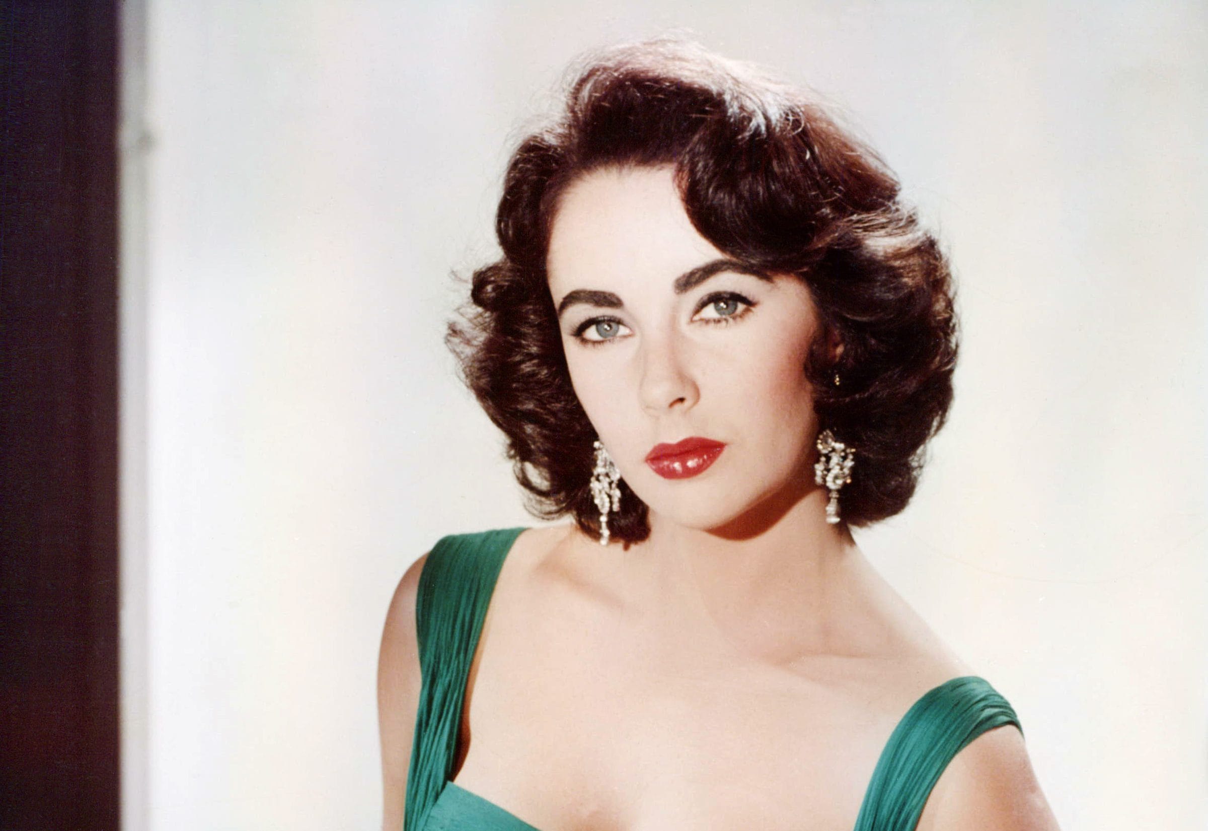 Woman with dark hair in green dress and earrings gazes softly, classic style portrait.
