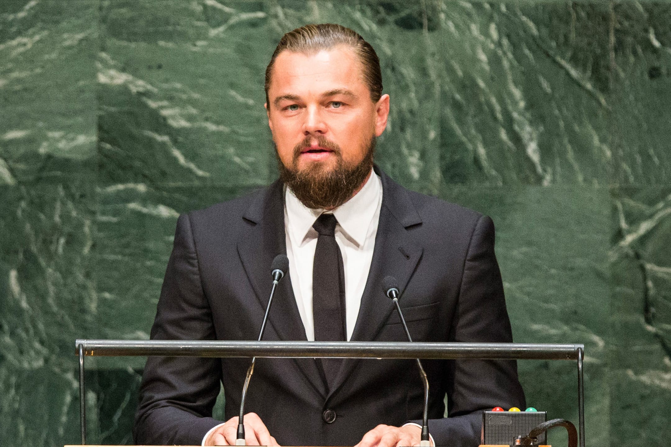 Man in a suit speaking at a podium against a marble background