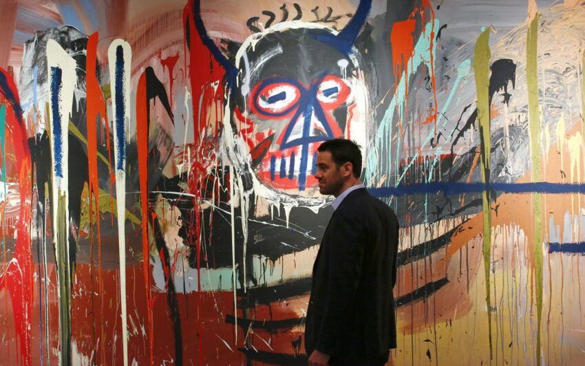 Man walks past a large street art mural featuring an abstract figure with horns and vibrant colors on display in a gallery.
