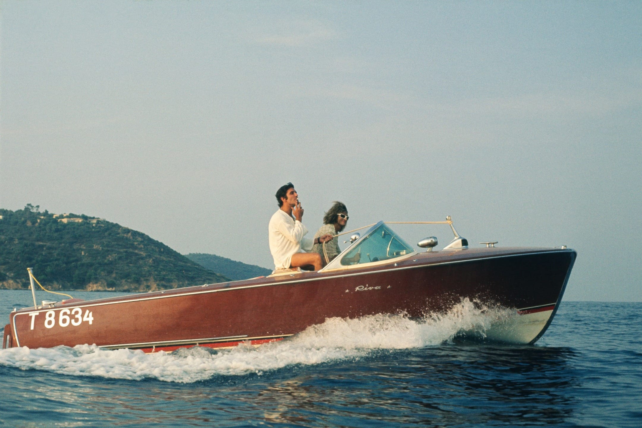 Man and dog enjoying a ride on a vintage speedboat with scenic coastline in the background.