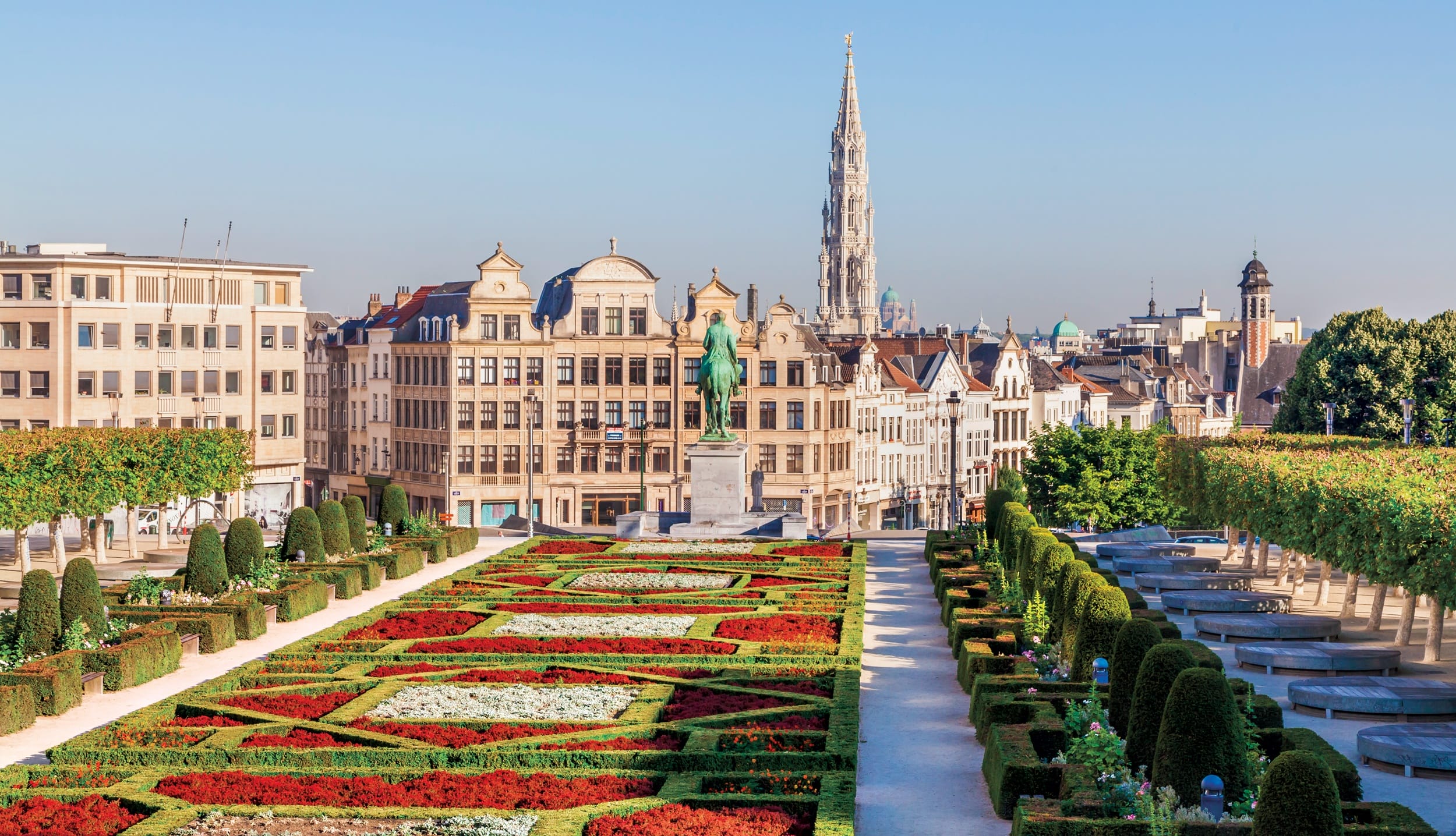 Scenic view of Mont des Arts garden in Brussels with vibrant flowerbeds and historic buildings in the background.