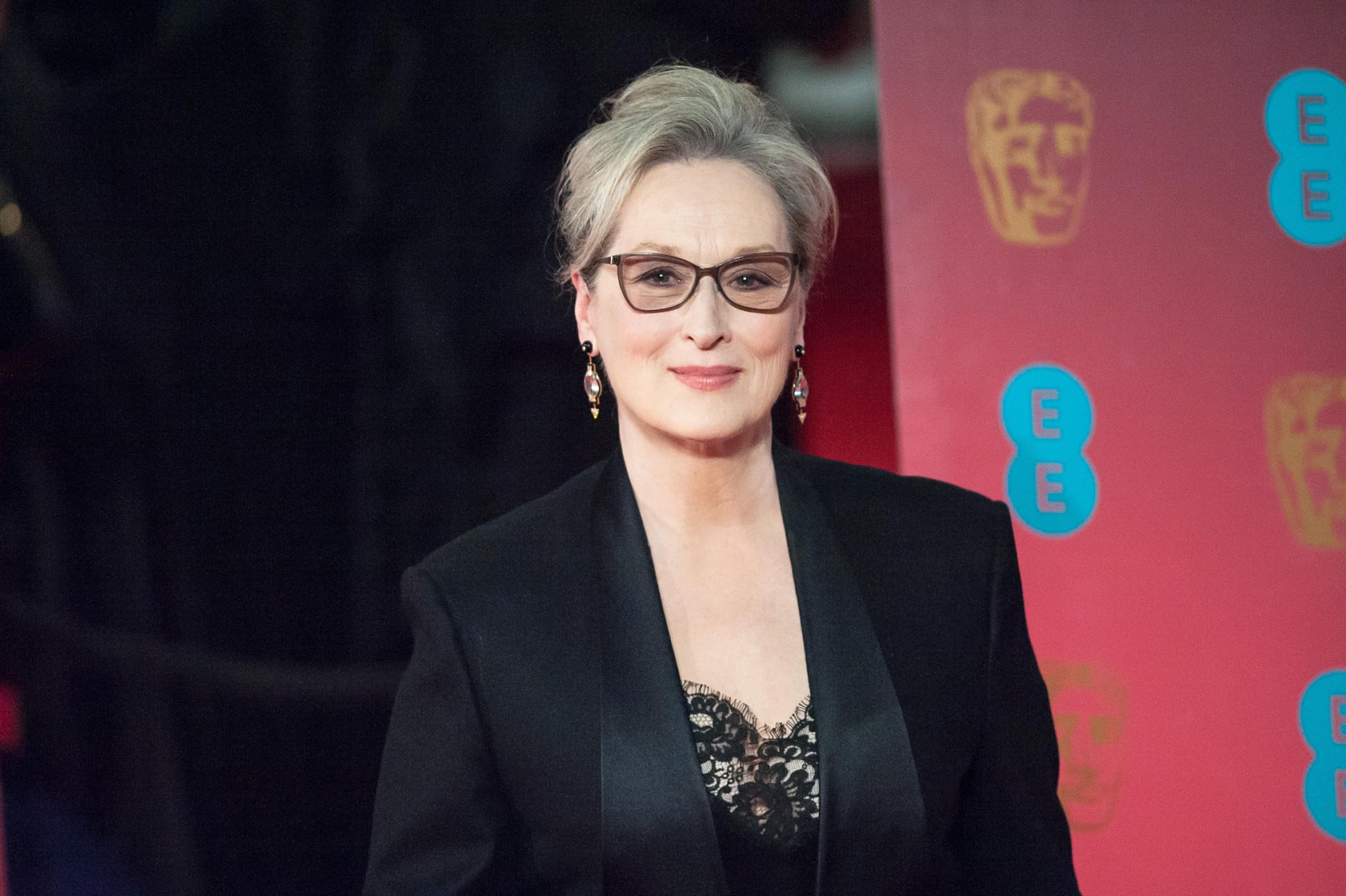 Person in formal attire on red carpet at an event with logos in the background.