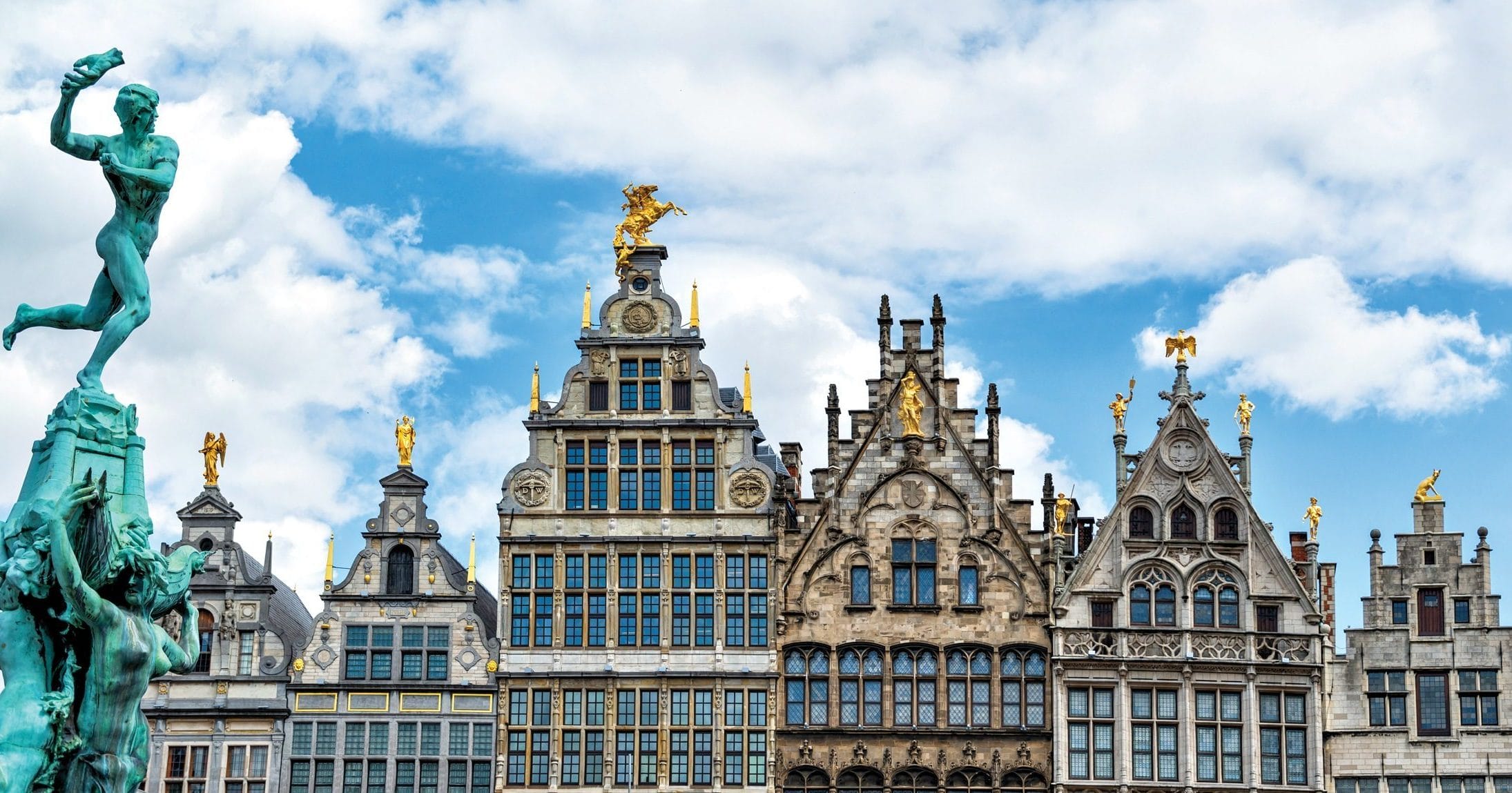 Ornate historic buildings and Brabo Fountain statue under a blue sky in Antwerp, Belgium.