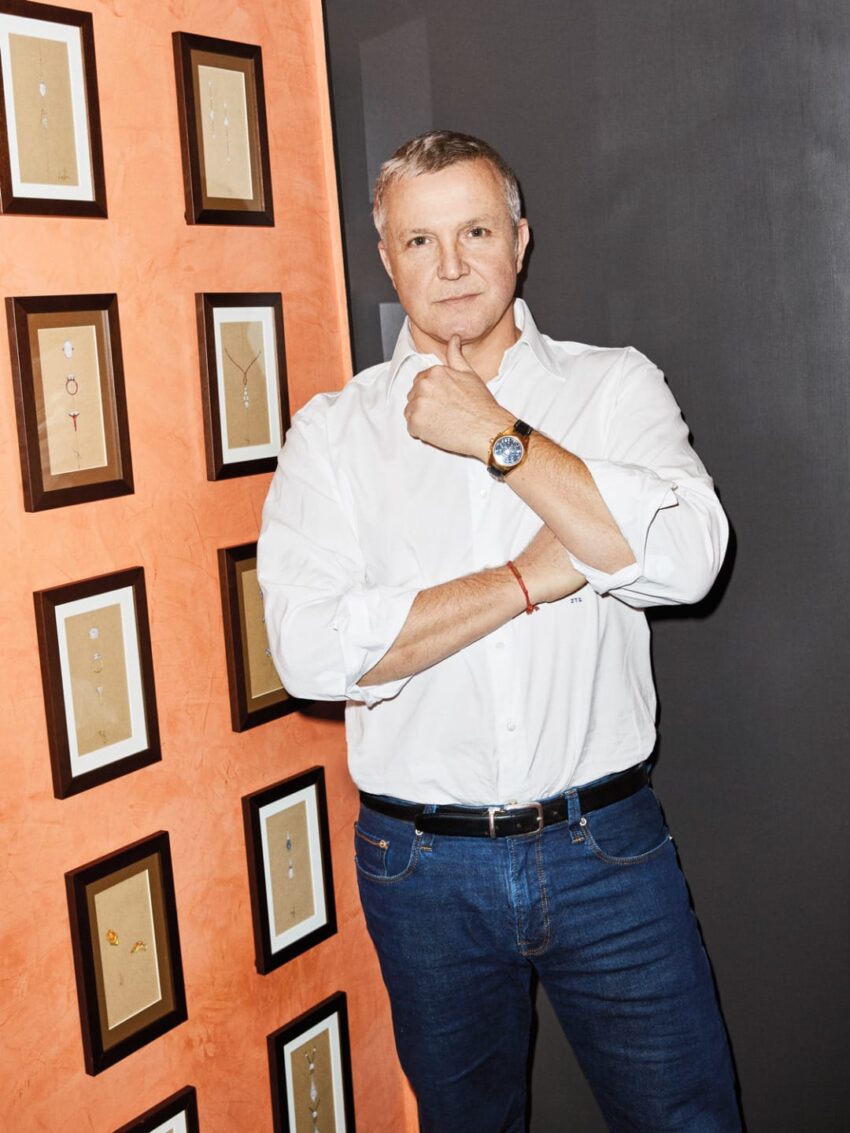 Man in white shirt and jeans stands next to a wall with framed art pieces.