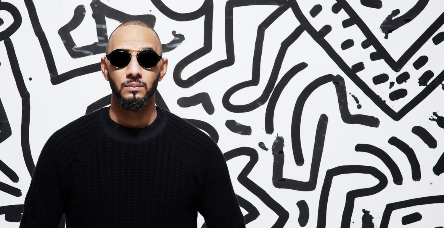 Man wearing sunglasses in front of a black and white abstract mural with geometric and wavy patterns.