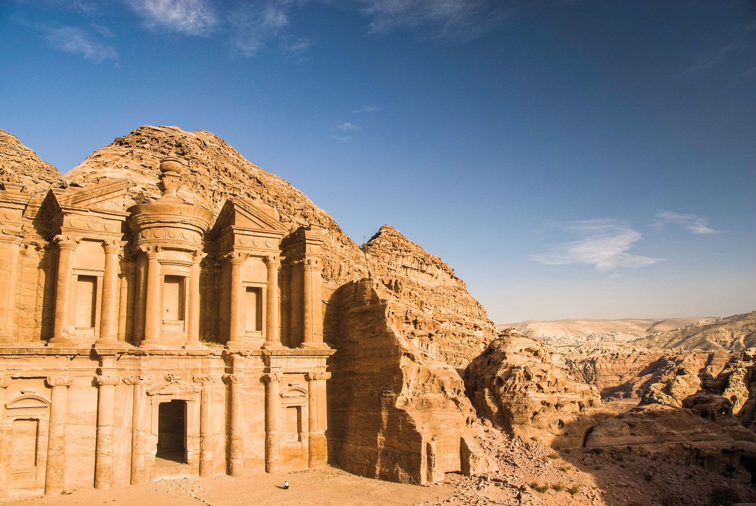 Ancient stone carved structure in Petra, Jordan with clear blue sky and rocky mountains in the background.