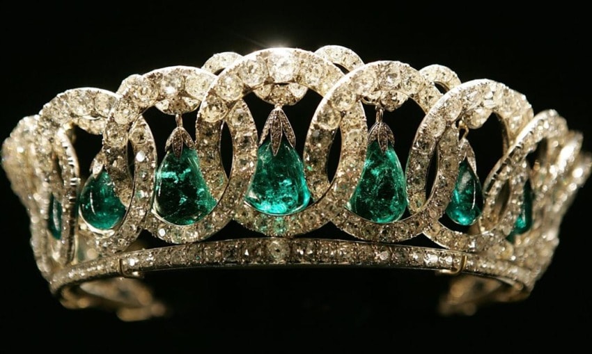 A sparkling diamond tiara with large green emeralds set against a dark background.