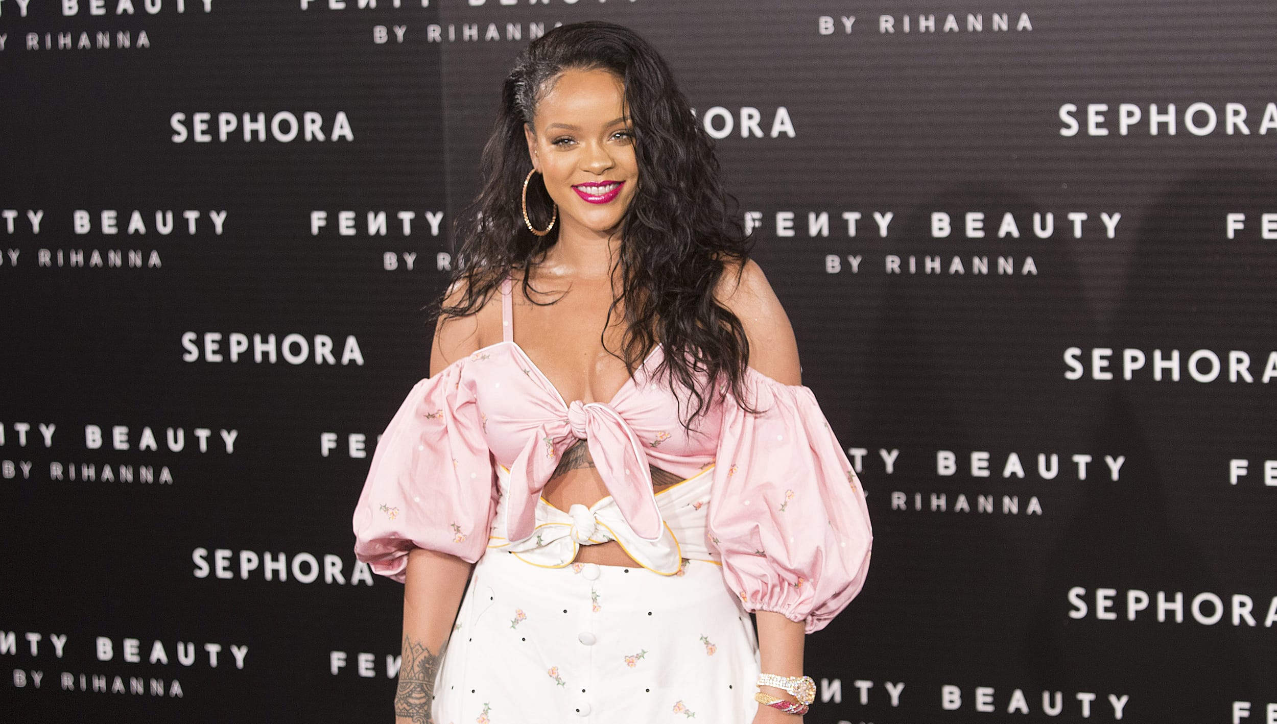 A person posing at a Fenty Beauty event wearing a pink top and white skirt.