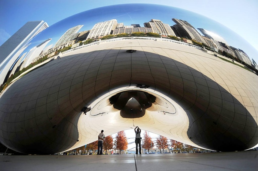 People standing under Chicago's reflective Cloud Gate sculpture with cityscape reflected on its surface.