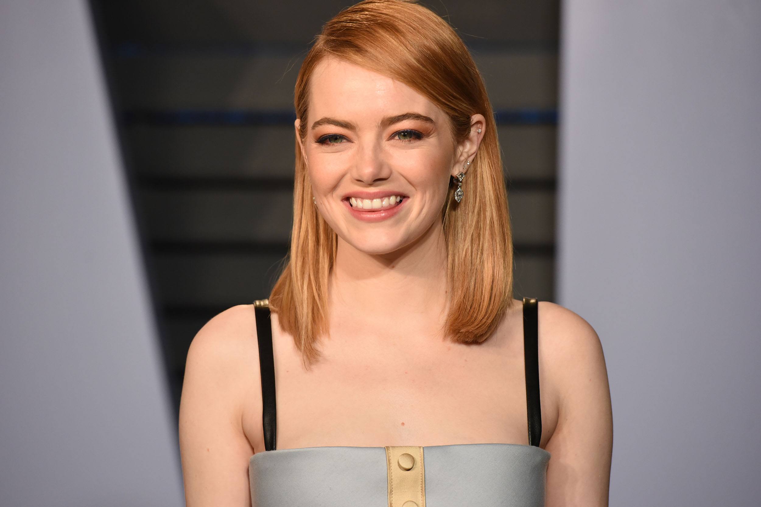 Smiling person with red hair wearing a sleeveless gray and black dress at an indoor event.