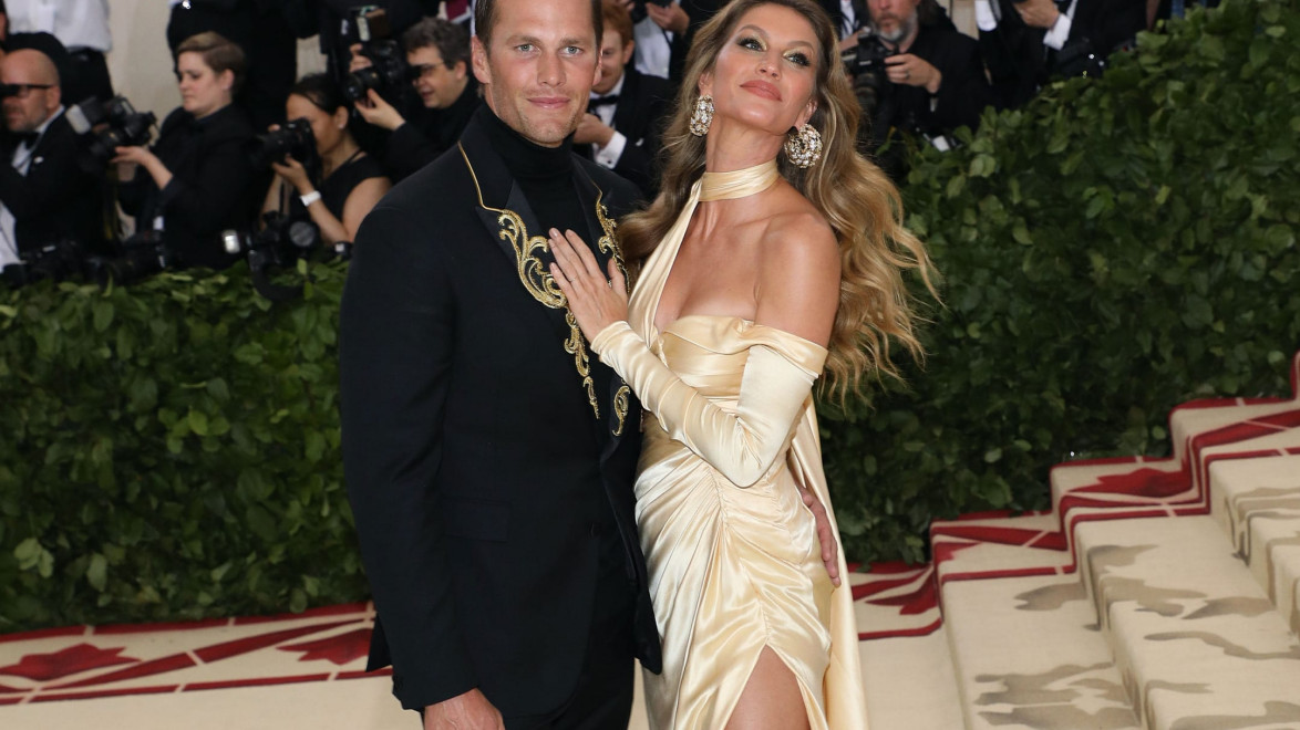A couple posing elegantly on a staircase at a formal event with photographers in the background.