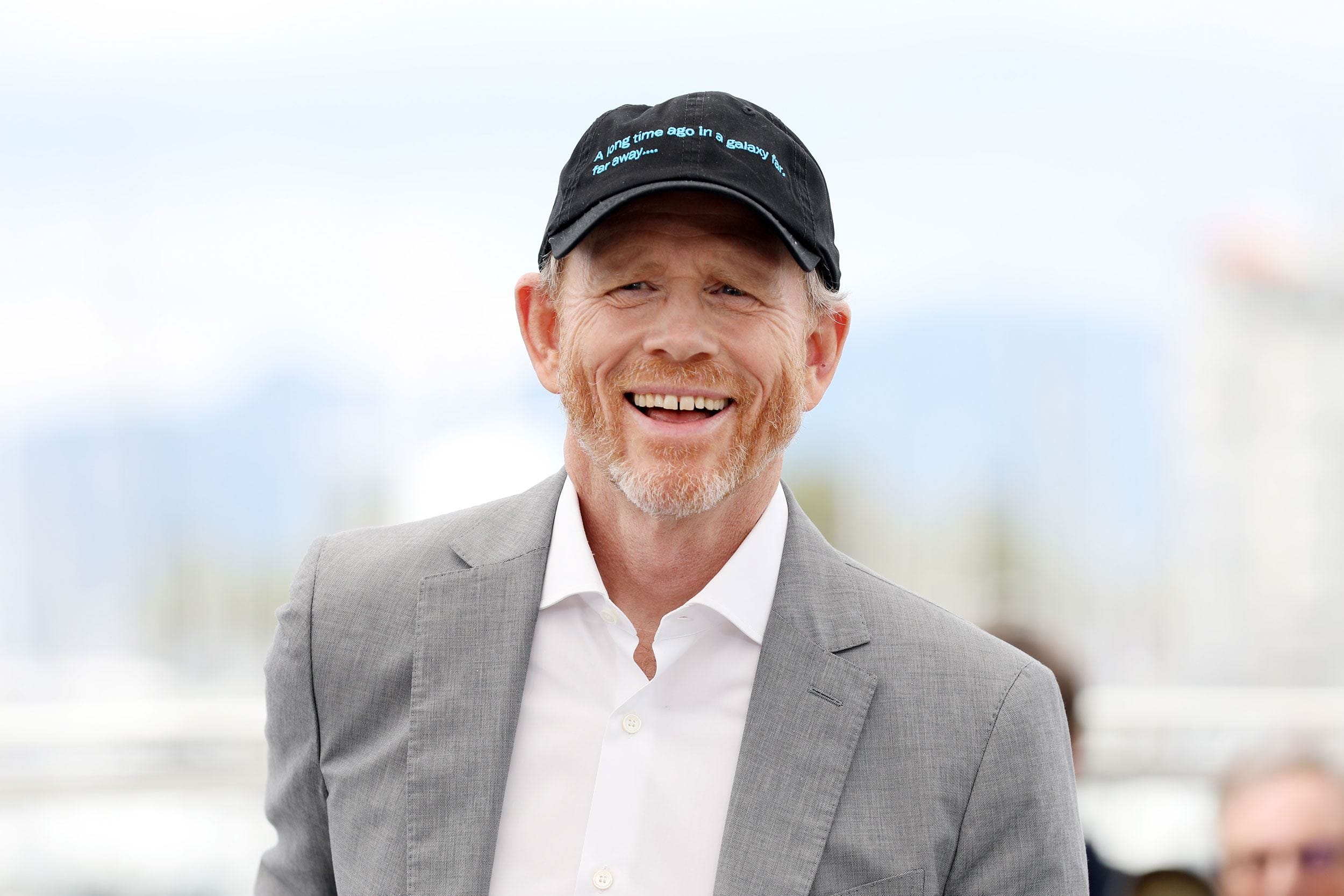 Man in a gray suit and black cap smiling outdoors.