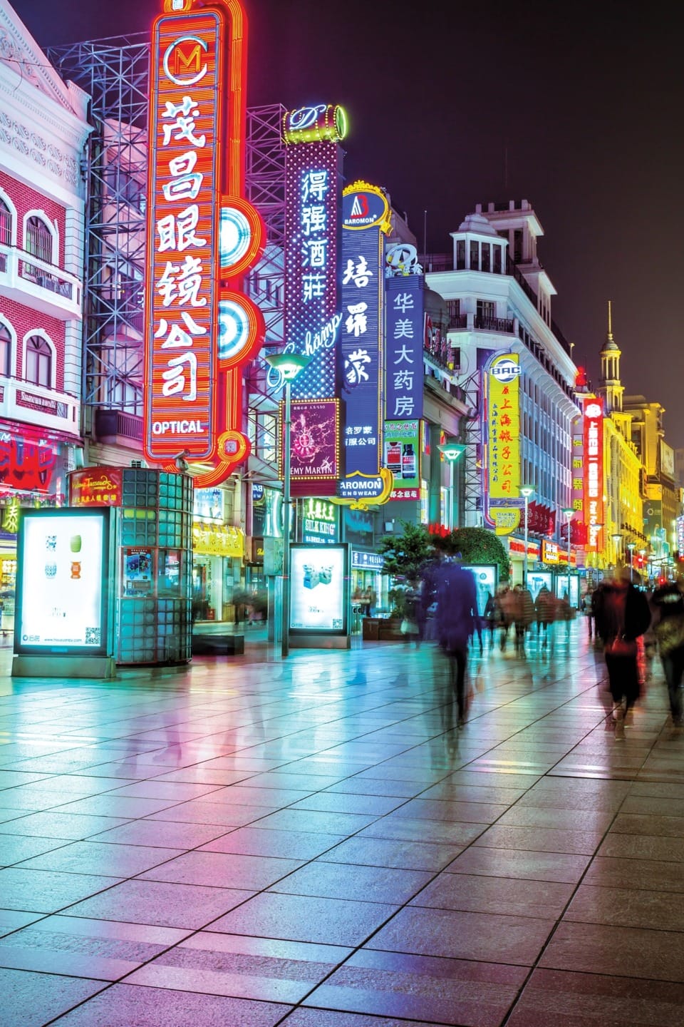Neon-lit street scene at night with colorful signs and people walking on a busy sidewalk.