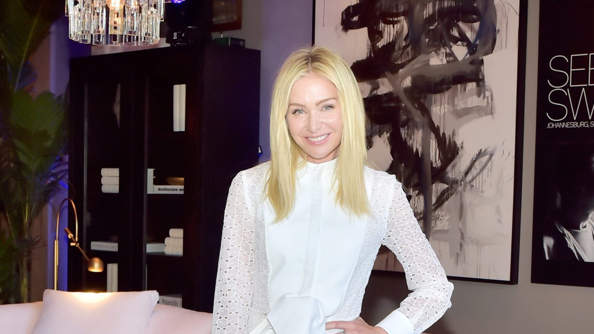 Person in a white dress standing in a stylish room with abstract art and a chandelier in the background.