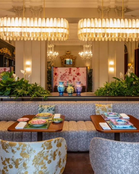 Elegant restaurant interior with plush seating, vibrant floral cushions, decorative vases, and chandeliers creating a cozy atmosphere.