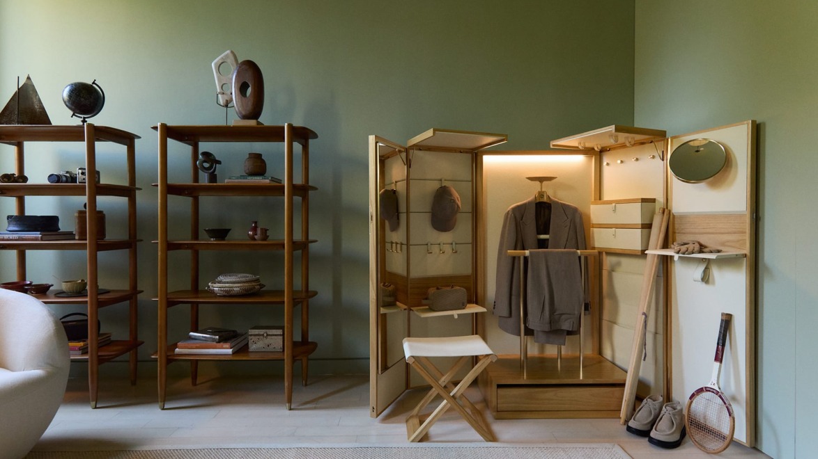 Modern room with wooden shelves displaying artifacts and a wardrobe cabinet with a hanging coat and mirror, in green tones.